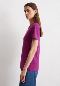 Paarse katoenen t-shirt met korte mouwen, ronde halslijn en een rechte snit, gecombineerd met blauwe denim jeans. De stof lijkt soepel.