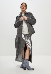 Chaqueta de lana gris con detalles de cremallera, falda maxi plateada metálica con una abertura delantera y botines de ante gris con tacón bloque.