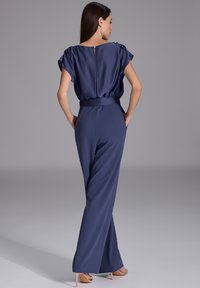 Combinaison bleu marine à manches courtes, taille cintrée et pantalons évasés. Texture satinée avec un détail en trou de serrure et une ceinture assortie.
