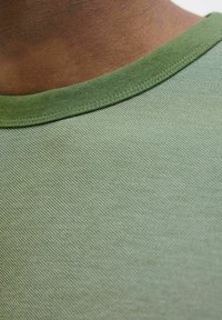 Camiseta verde de cuello redondo con un tejido de algodón texturizado, vista en primer plano que destaca el cuello y la superficie suave.
