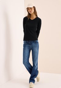Svart långärmad V-ringad topp i kombination med blå jeans och beige sneakers, kompletterad med en ljusfärgad keps. En enkel och avslappnad design.