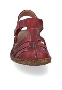 Sandale en cuir rouge avec un bout fermé, des côtés ouverts et une sangle réglable. Présente des coutures beiges et une semelle brune texturée.