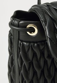 Schwarze Ledertasche mit gewebter Textur, goldfarbenen Beschlägen und Kordelzugverschluss. Das Material wirkt glatt und langlebig.