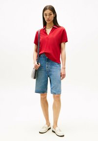 Polo shirt rosso a manica corta con scollo a V, abbinato a pantaloni corti di jeans azzurri. Accessoriato con una piccola borsa a motivo e mocassini.