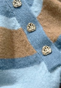Cardigan en laine mélangée douce avec un motif géométrique bleu et marron, orné de boutons en forme de nœud en métal argenté.