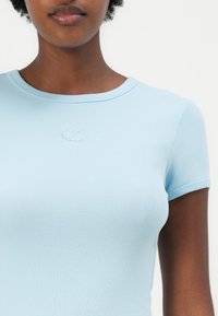 Light blue short-sleeve top, ribbed texture, round neckline, embroidered CK logo at the chest, fitted design.