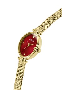Orologio da polso dorato con quadrante rotondo rosso, quattro indici orari quadrati, un accento in cristallo e un bracciale in maglia dorata. Chiusura regolabile.