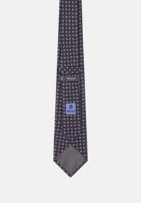 Brūns zīda kaklasaite ar ģeometrisku zilu un baltu rakstu, ar vienkrāsainu tumšu apakšpusi un zīmola etiķeti, kas izšūta priekšpusē.