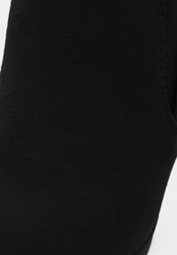 Botín negro con textura similar al ante, punta afilada y panel lateral elástico para facilitar su colocación. Sin herrajes o acentos visibles.