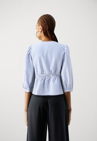 Blå og hvit stripete bluse med korte pufferm, smockede midjedetaljer og rund hals, sammen med svarte vide bukser.