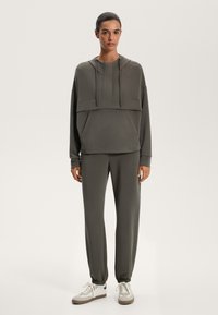 Oliven grøn hoodie og matchende sweatpants i blødt stof, med en kængurulomme, snore og elastiske manchetter. Sneakers med hvide og beige accenter.