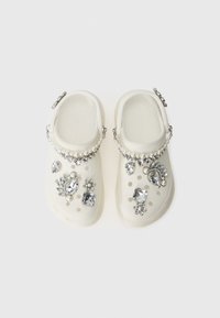Vita hartsandalor i vit resin med dekorativa silver- och klara stenar, pärlor och olika utsmyckningar på den övre ytan.