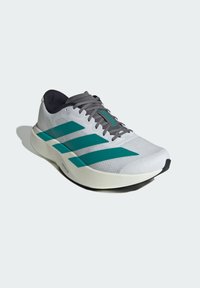 Scarpa da corsa con tomaia in rete bianca, tre strisce teal, lacci grigi e una suola imbottita color avorio. Dettagli texturizzati sulla tomaia.