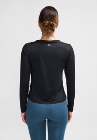 Czarna sportowa bluzka z długim rękawem, okrągłym dekoltem i fakturowaną tkaniną. Z tyłu drobny detal z logo. W zestawie z niebieskimi legginsami.