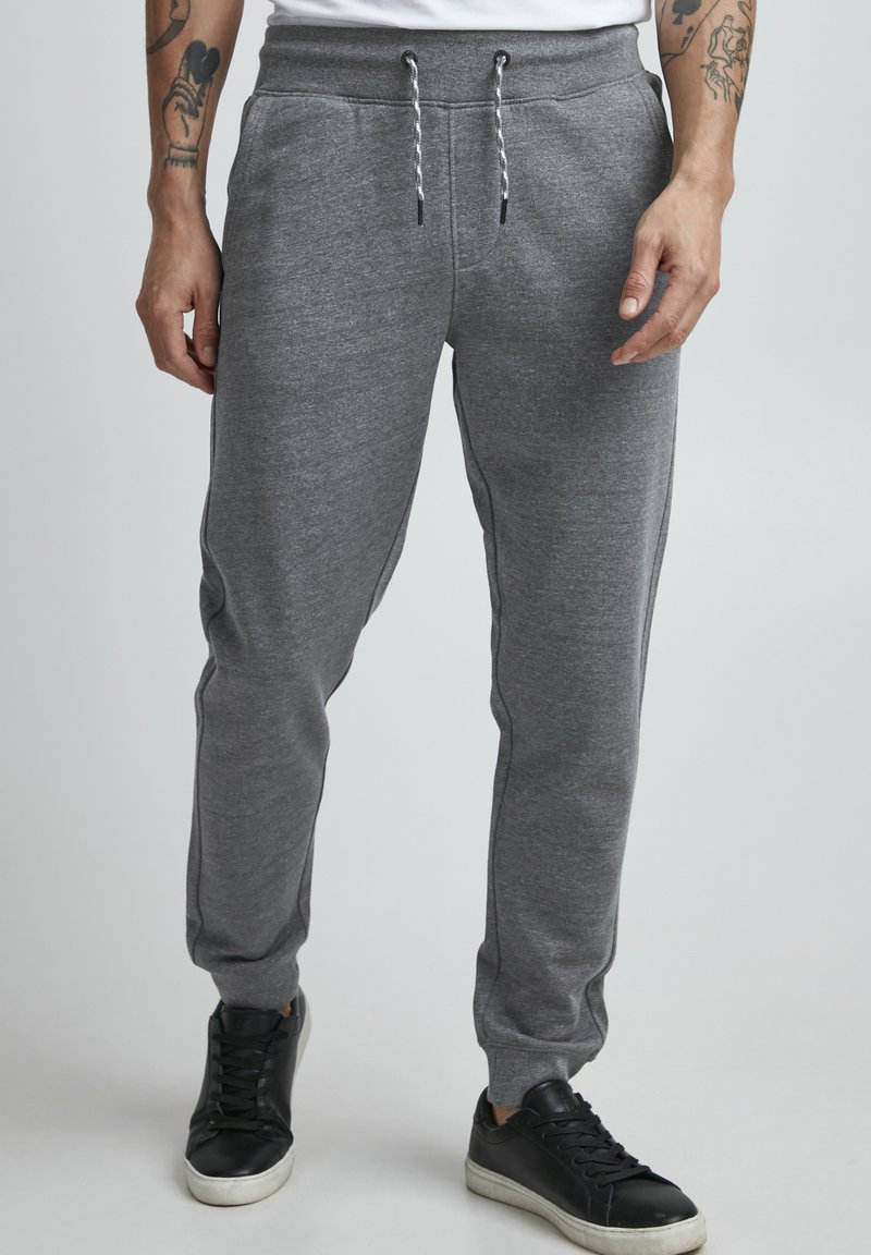 Grå joggebukser laget av myk stoff, med elastisk midjebånd, snøre, sidelommer og tilpassede ankler.