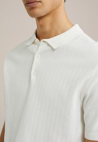 Cămașă polo tricotată albă, cu guler, având un model texturat în zigzag și trei butoane pe placket.