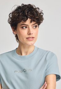 Ljusblå t-shirt med kort ärm i mjuk bomull, med rundad halsringning och silverbroderad "Polo Club"-logotyp på bröstet.