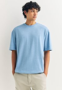 Jasnoniebieska bawełniana koszulka z krótkimi rękawami i okrągłym dekoltem, o luźnym kroju i gładkiej teksturze. Widoczny subtelny melanżowy wzór.