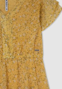 Keltainen kukallinen mekko, joka on valmistettu kevyestä kankaasta, lyhyillä hihoilla, V-päällä ja joustovartisella vyötäröllä. Mekko sisältää hajallaan olevia valkoisia ja vihreitä kukkakuoseja.