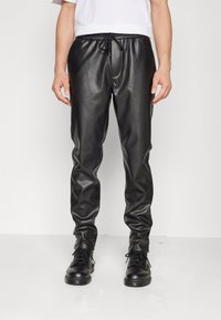 Zwarte faux leren joggers met elastische tailleband, trekkoordsluiting en taps toelopende benen. Gepaard met zwarte veterschoenen.