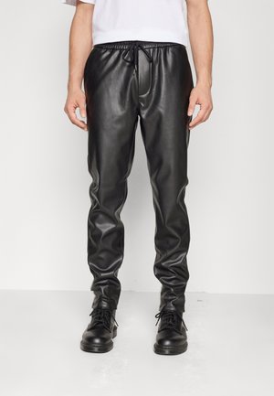 Black faux leather joggers with elastic waistband, drawstring closure, and tapered legs. Paired with black lace-up boots.