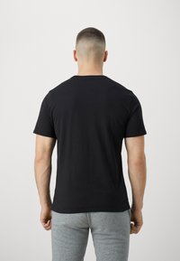 Zwarte T-shirt met korte mouwen, gemaakt van katoen. Kenmerkt zich door een ronde halslijn en een eenvoudig ontwerp. Van achteraf gezien, gedragen met grijze trainingsbroeken.