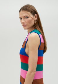 Färggad stickad klänning med horisontella ränder i blått, rött, grönt, rosa och glittrande brunt, med ärmlös design och djupa sidokutt.