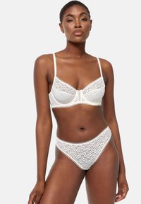 Brassière en dentelle blanche avec motif floral, bonnets doux, bretelles réglables, et culotte haute assortie avec bords festonnés.