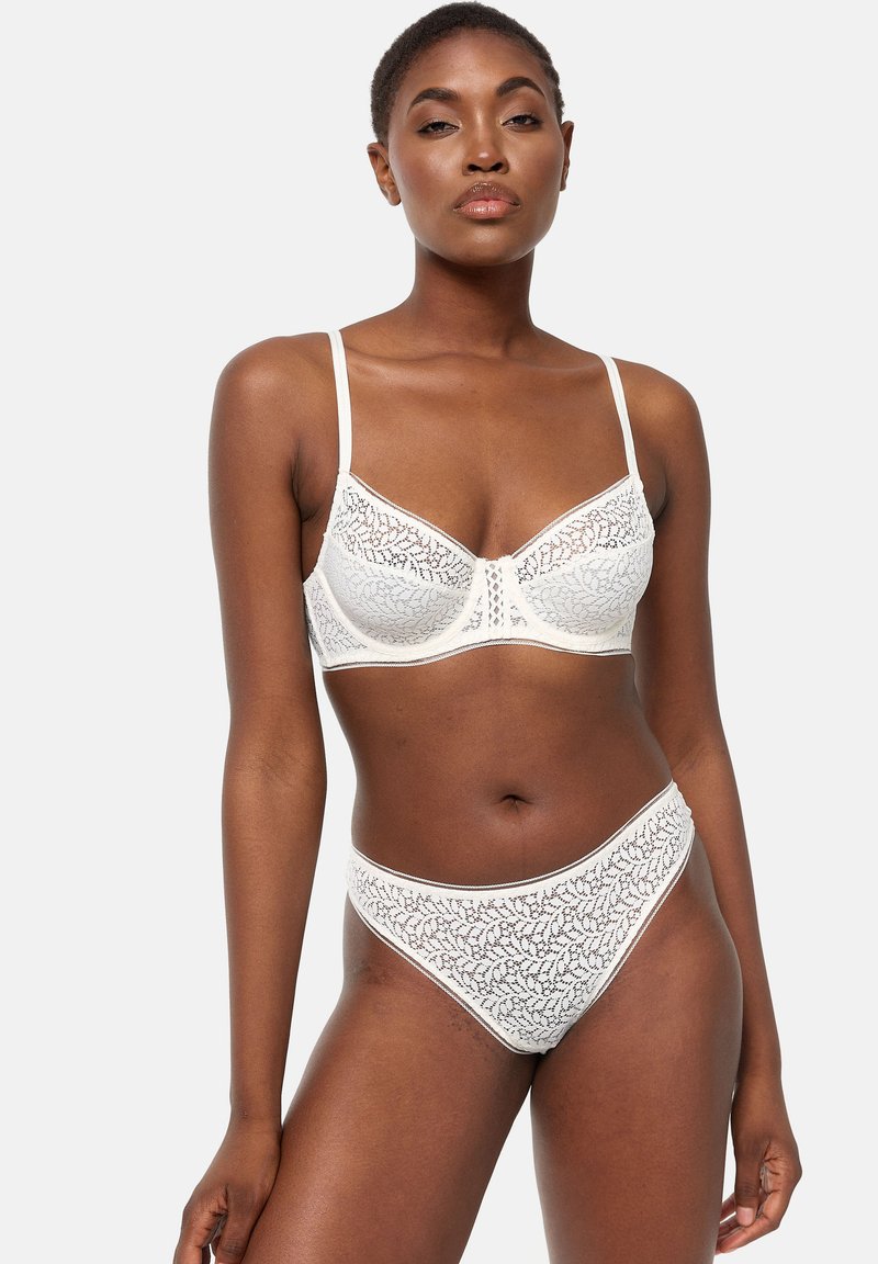 Brassière en dentelle blanche avec motif floral, bonnets doux, bretelles réglables, et culotte haute assortie avec bords festonnés.