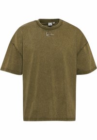 Olivově zelené oversized tričko, krátké rukávy, žebrovaný výstřih, jemná textura, na hrudi má malou vyšívanou nášivku.