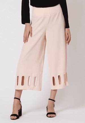 Mujer con pantalones anchos rosa pálido recortados con cortes verticales cerca del dobladillo y tacones negros con tiras en el tobillo.