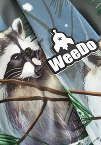 Mångfärgad tyg med illustrationer av tvättbjörnar bland tallgrenar, med en svart och vit "WeeDo"-logotyp som är väl synlig.