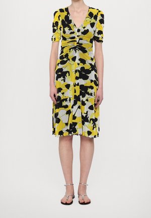 Robe fleurie jaune avec des motifs noirs et gris, dotée de manches courtes bouffantes, d'un décolleté en V et d'une taille froncée. Tissu lisse avec un ourlet.