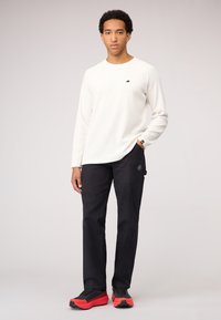 Biała prążkowana koszulka z długim rękawem, czarne spodnie i czarno-czerwone trampki. Dyskretny logo na koszulce i okrągłe logo na spodniach. Casualowy krój.