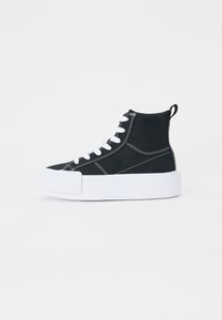 Svart høyhælte sneakers laget av lerret med hvite sømmer og snøring. Har en tykk hvit gummisåle og en bakre trekkstang.