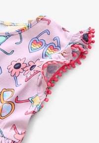 Fialový bavlněný top s barevnými slunečními brýlemi a květinovými potisky, zakončený růžovým lemováním s bambulkami na okrajích rukávů.