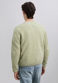 Suéter verde de lana con acabado texturizado, puños y dobladillo acanalados, con un diseño clásico de cuello redondo. Combina con jeans azul claro.
