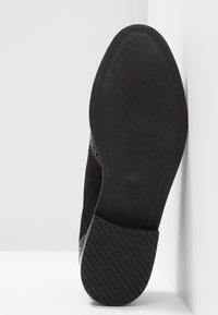 Semelle d'une chaussure habillée en cuir noir avec l'avant lisse, le talon texturé et un logo embossé sur la semelle extérieure en caoutchouc lisse.