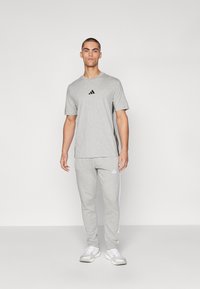 Tenue de sport grise composée d'un t-shirt à manches courtes et d'un pantalon, avec un logo noir et des rayures blanches sur les côtés.