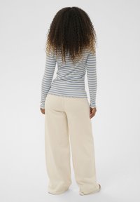 Langærmet top med blå og hvide striber og bølget kant, kombineret med løstsiddende beige bukser med en blød tekstur og vide ben.