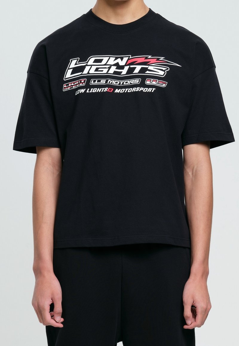 T-shirt en coton noir avec un motif graphique en texte blanc et rouge. Manches courtes, coupe décontractée et col rond.