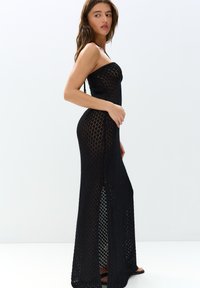 Robe maxi noire en tricot à coupe régulière, présentant un motif diamond texturé, des fentes latérales et des bretelles fines pour une silhouette ajustée.