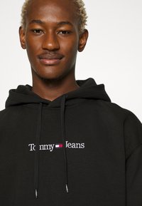 Felpa nera in cotone, con il logo "Tommy Jeans" ricamato in bianco con accenti rossi e blu, con cappuccio e una vestibilità casual.