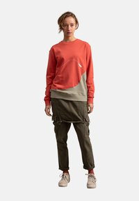 Rode en olijfgroene sweatshirt met een wit abstract ontwerp, ronde halslijn en ribgebreide manchetten. Gecombineerd met olijfgroene cargobroek met ritsen.