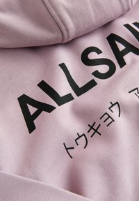 Tissu de sweat à capuche rose avec texte en gras noir "ALLSA" et petits caractères japonais imprimés en dessous.