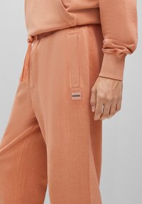 Helle Pfirsich-Jogginghose aus weichem Stoff, mit einem Kordelzugbund, seitlichen Taschen und einem kleinen HUGO-Logo-Patch am Oberschenkel.