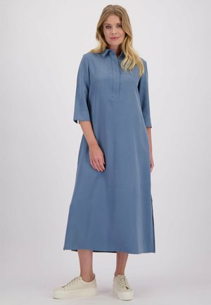 Lichtblauw, knielang jurkje met een kraag, driekwart mouwen en zijsplitten. Gemaakt van een soepele stof. Gedragen met lichte sneakers.