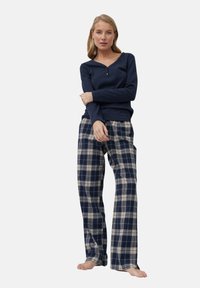 Top de manga larga azul marino con escote tipo henley y detalle de botones, combinado con pantalones de pierna ancha de cuadros en azul oscuro y crema. Textura suave.