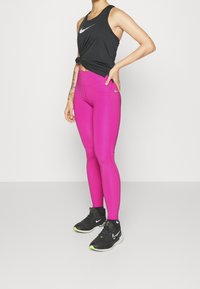 Top nero senza maniche, leggings rosa e scarpe da atletica nere con accenti verde neon. I leggings hanno una vestibilità aderente e una texture liscia.