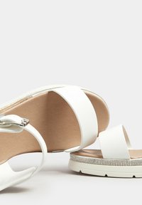 Białe sandały z grubym obcasem, z gładkimi skórzanymi paskami i błyszczącym akcentem na podeszwie. Wyposażone w wyściółkę dla komfortu.